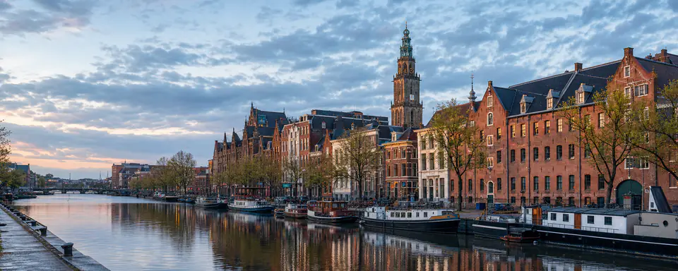 Illustrated view of Groningen's canal with brick warehouses, houseboats, and the Martinitoren in evening light