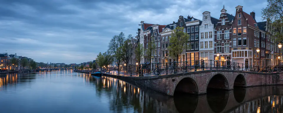 Illustrated panorama of an Amsterdam canal with arched bridges and historic gabled houses at dusk