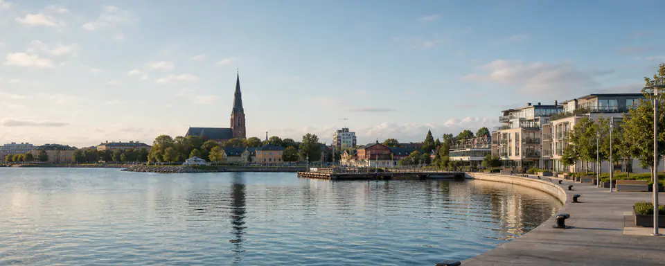 Illustrerad vy över Västerås hamn med kyrkspira, äldre stadskvarter, moderna bostadshus och lugnt vatten