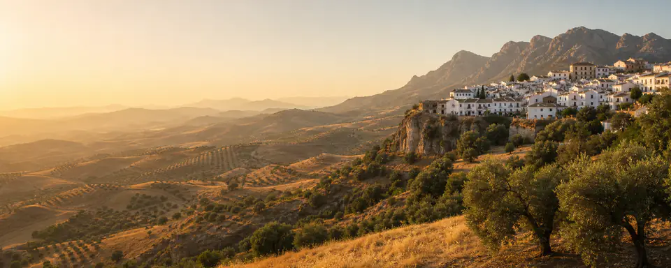 Illustrated Spanish mountain landscape with a white village, olive groves, and warm evening light